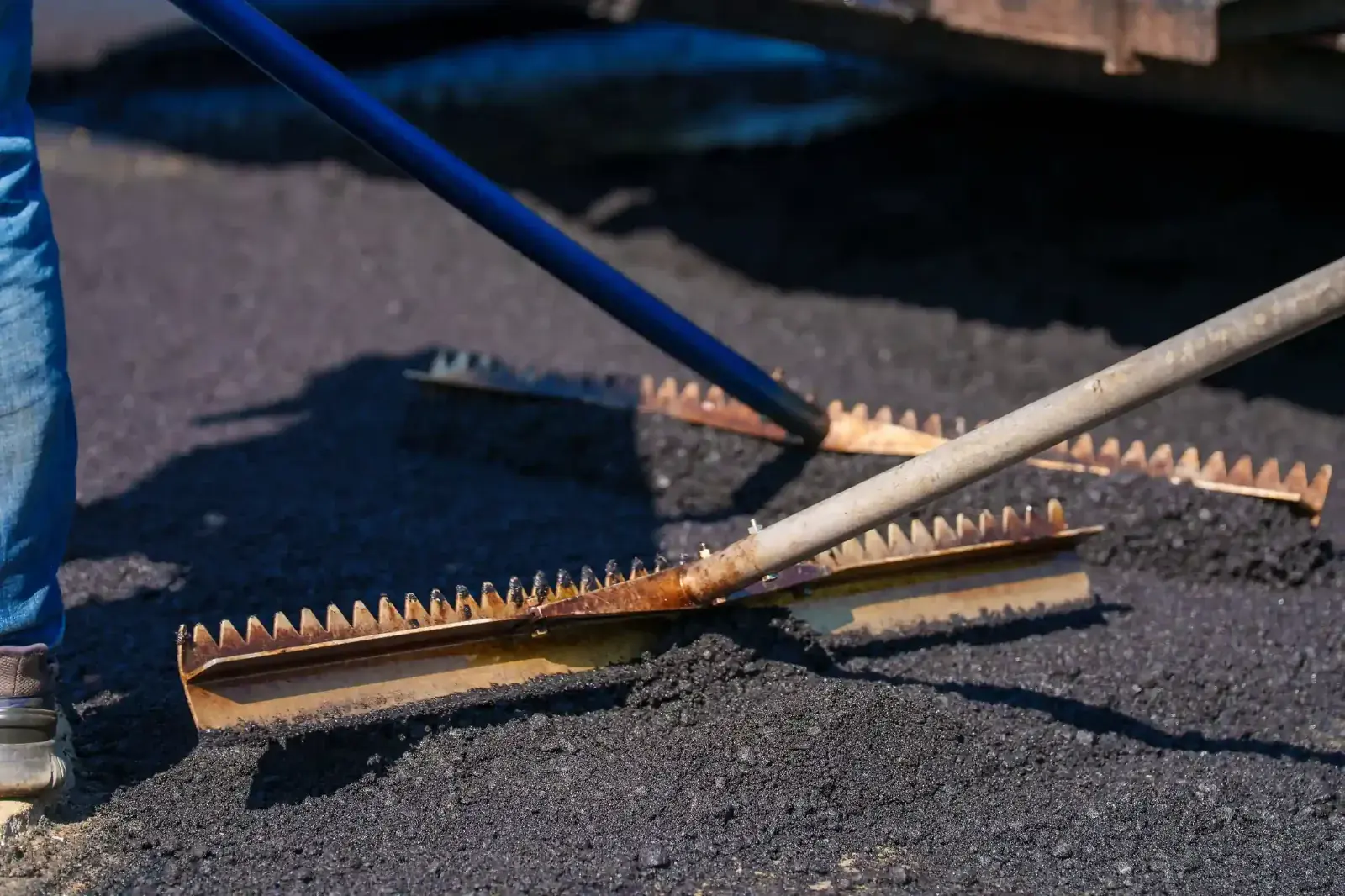 Crew member finishing fresh asphalt with a lute rake
