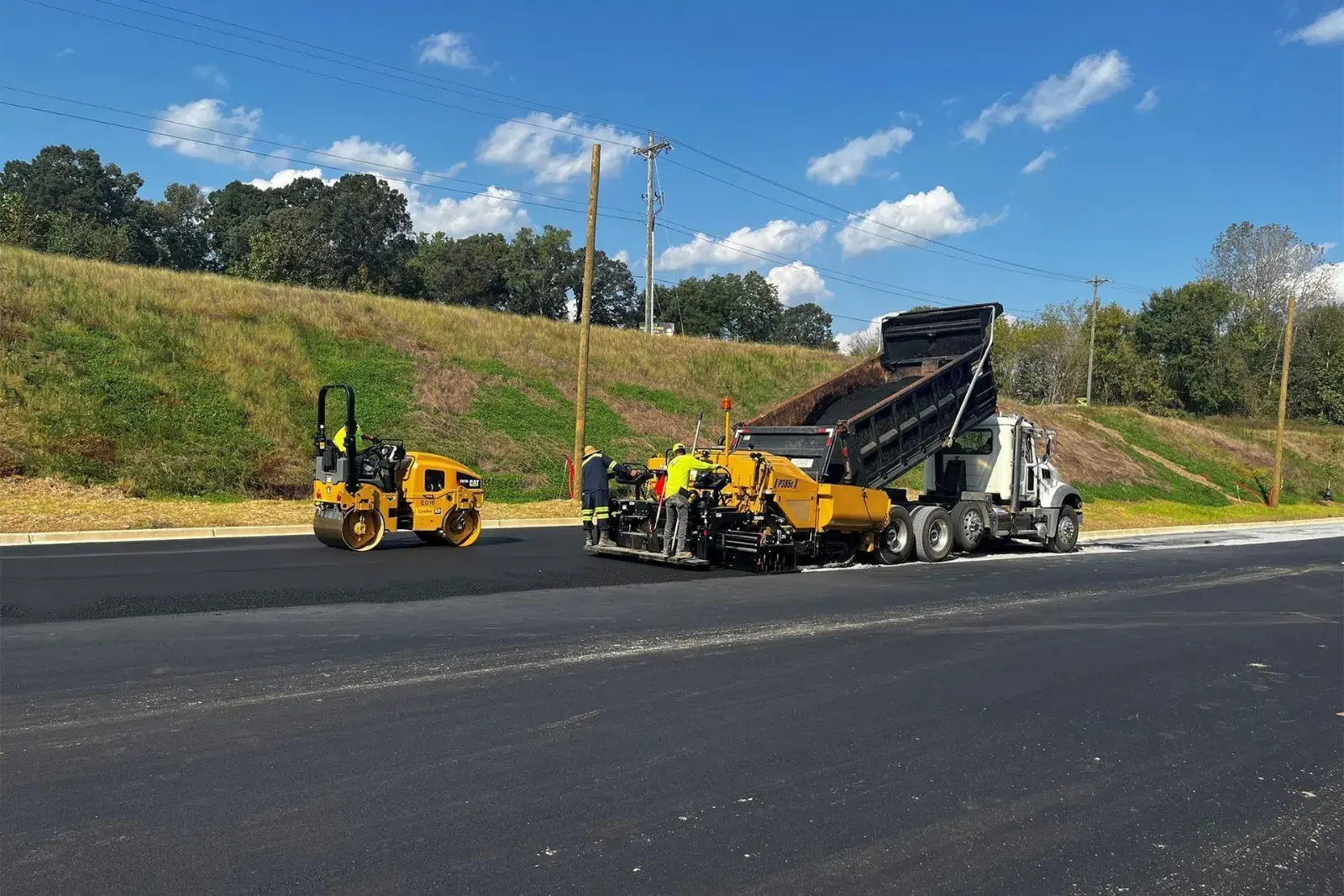 Paver, roller and dump truck paving a commercial parking lot