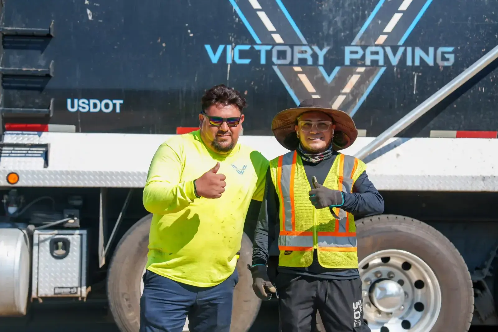Victory Paving crew members giving a thumbs up beside a company dump truck